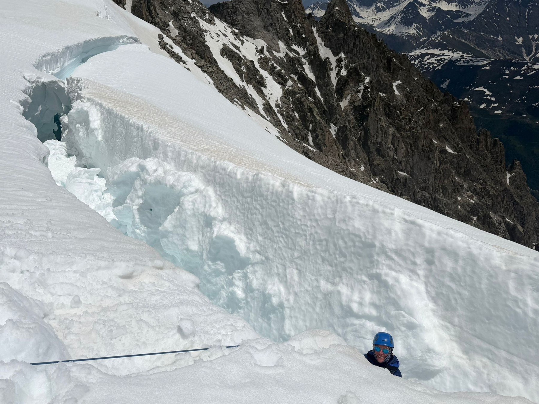 Erica Stanford in a blue helmet at the edge of a large crevasse below the summit of Mont Blanc, with the ice wall and the rope running across the snow, during crevasse rescue training