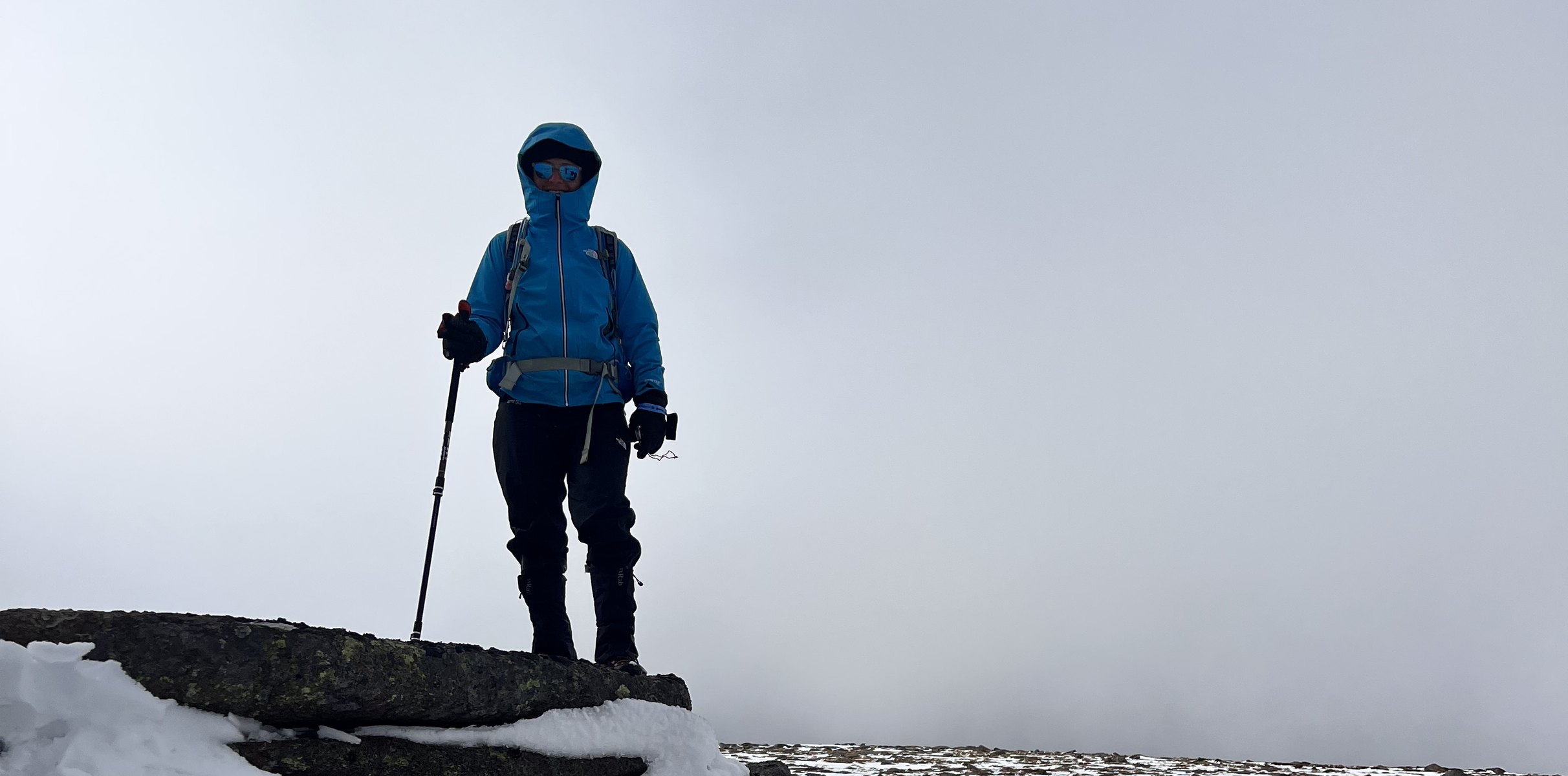 Erica Stanford standing on a snowy summit rock in the Cairngorms in winter, in cloud