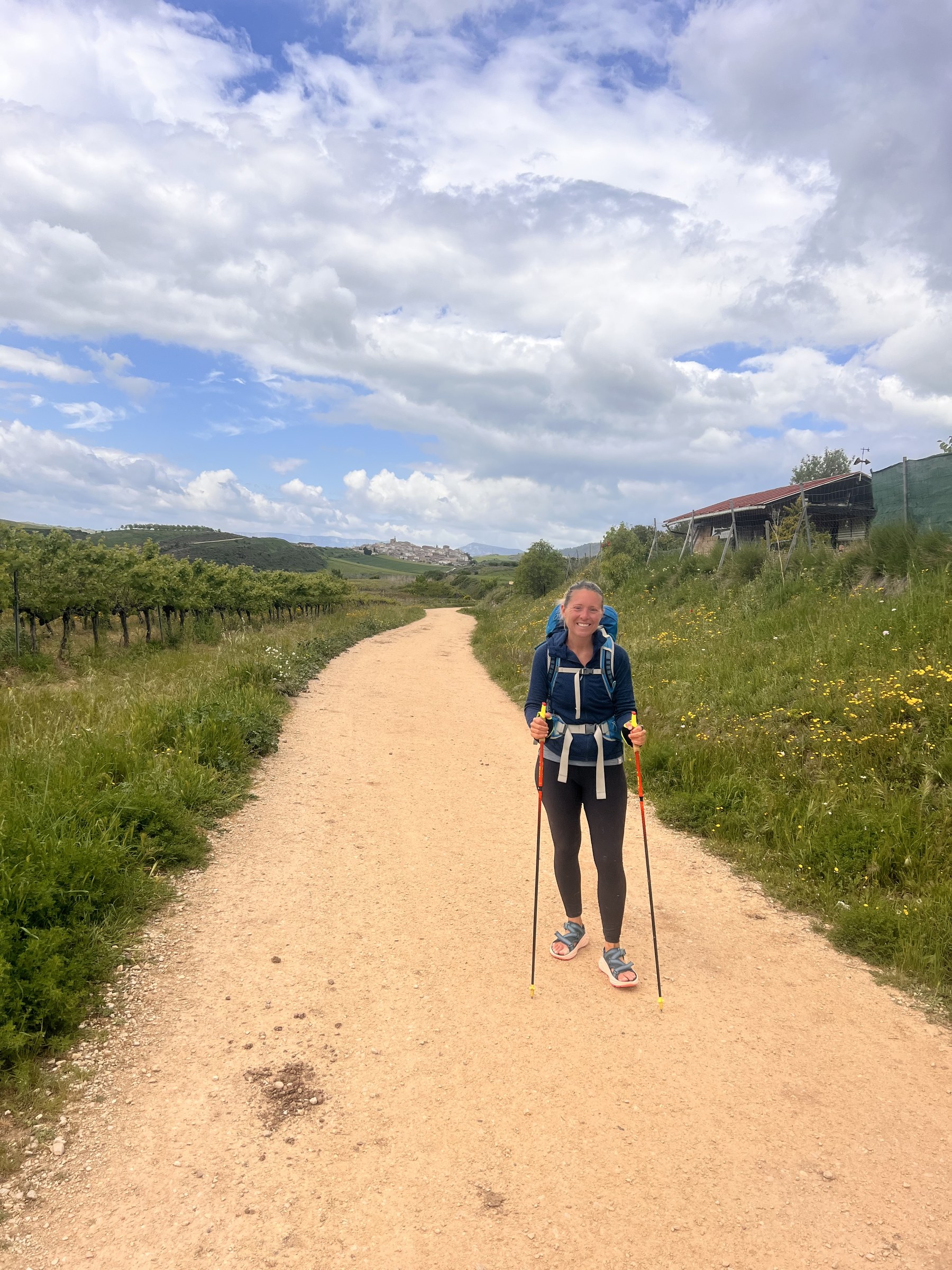 Erica Stanford walking the Camino de Santiago with walking poles on a track through the hills