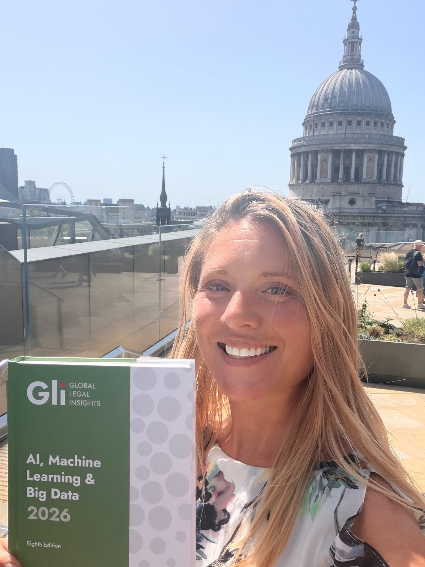 Erica Stanford holding Global Legal Insights AI, Machine Learning and Big Data 2026, which she contributed to, with St Paul&rsquo;s Cathedral behind