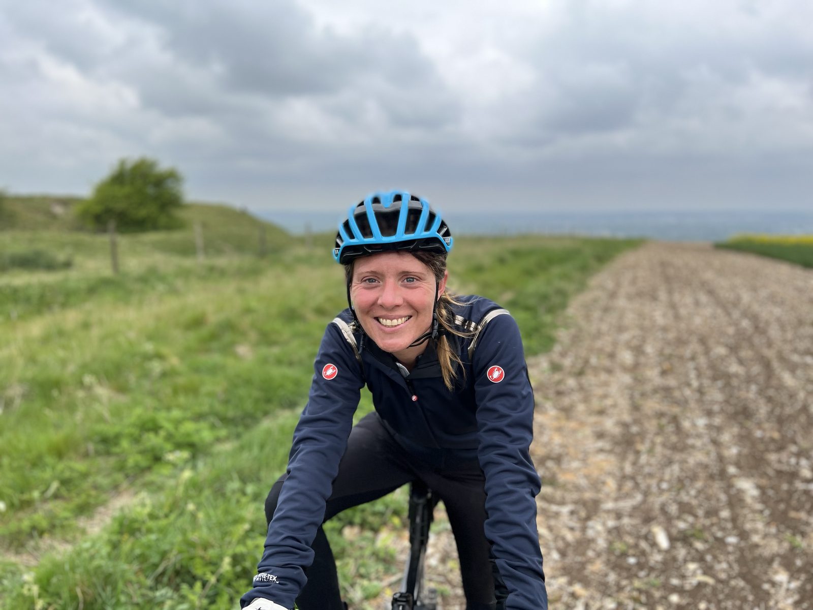 Erica Stanford on her gravel bike on a chalk track with fields and hills behind