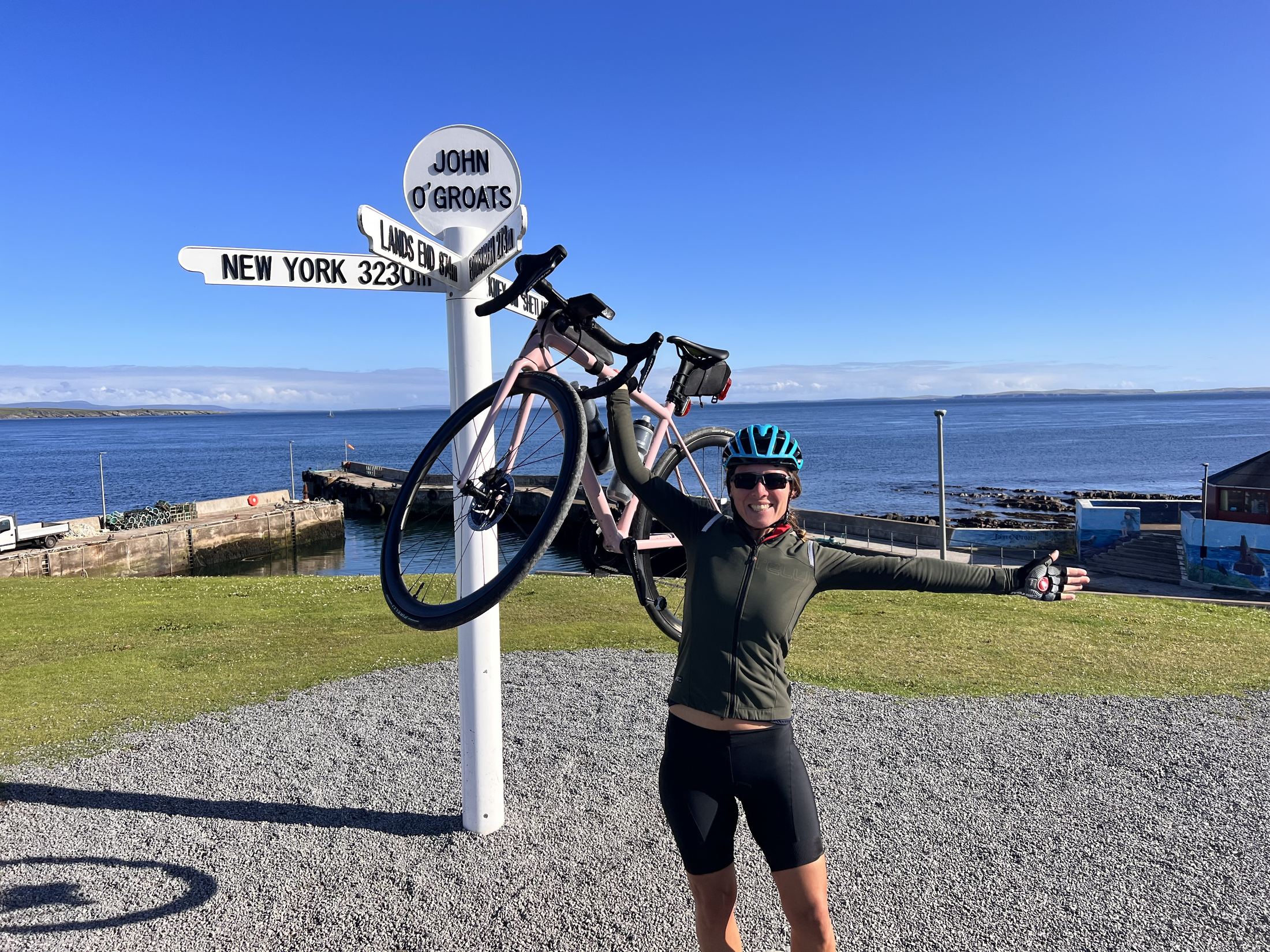 Erica Stanford holding her bike above her head at the John O'Groats signpost in northern Scotland