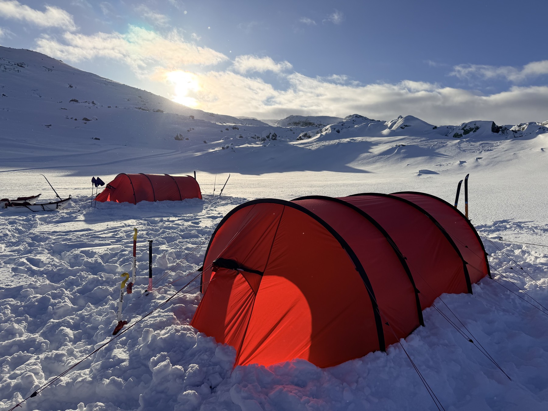 Two red expedition tents pitched in the snow at Finse in Norway, with pulks and skis beside them and low sun over the plateau, during polar expedition and survival training